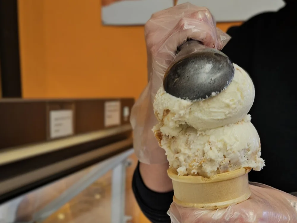 A scoop being dipped by hand into a waffle cone at the counter