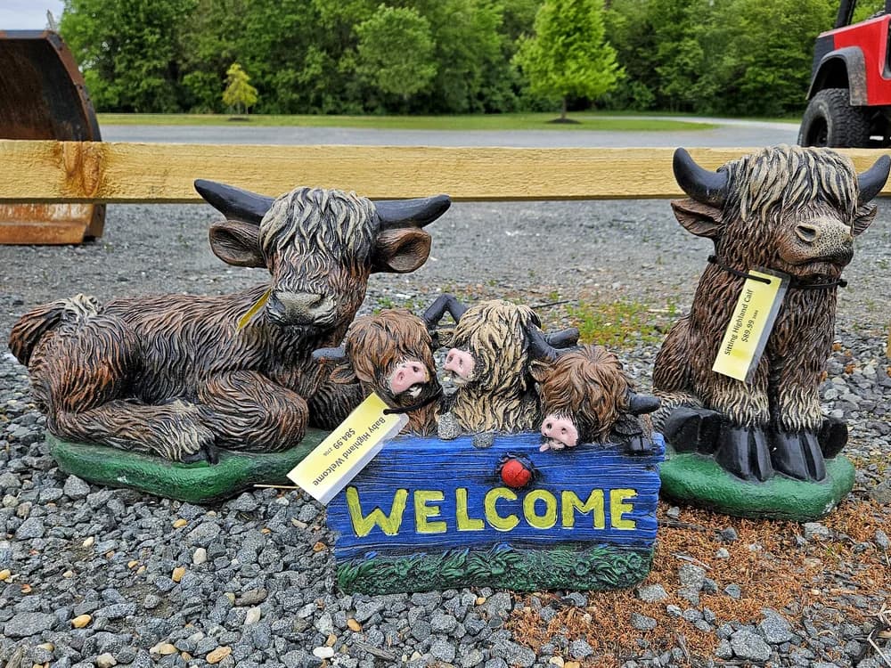 Concrete highland cows and calves around a welcome sign