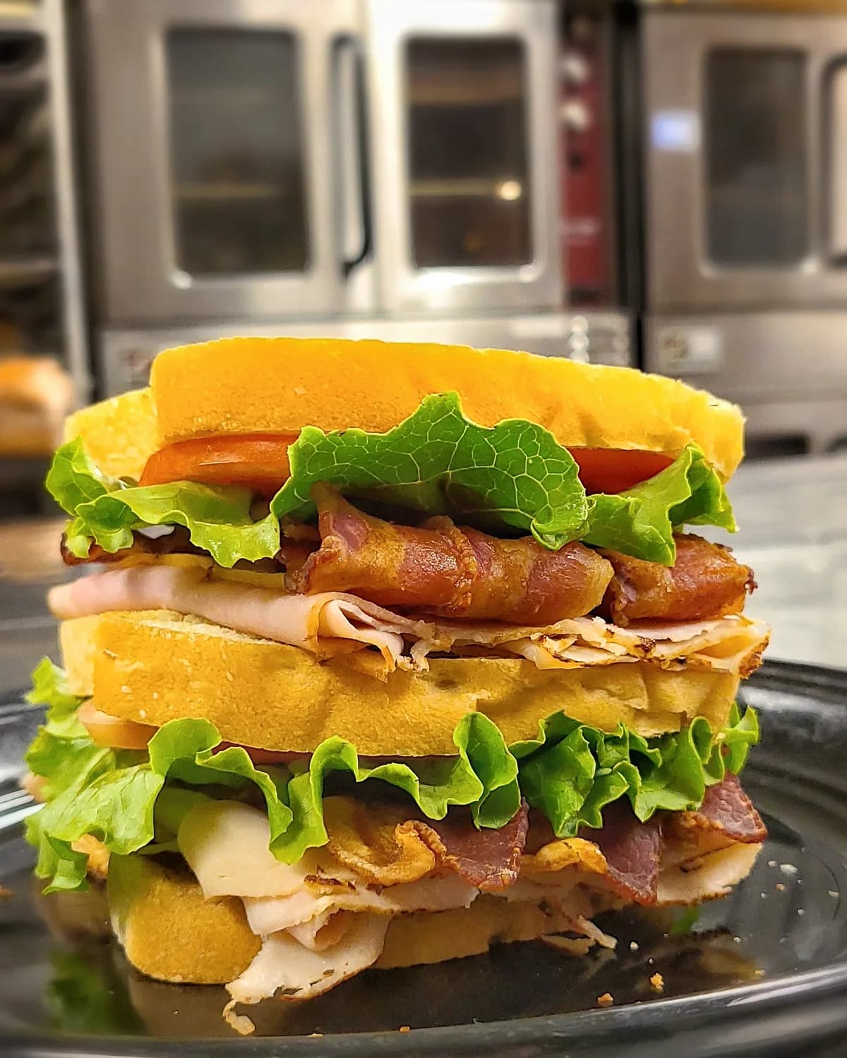 A stacked club sandwich on a plate in the store kitchen